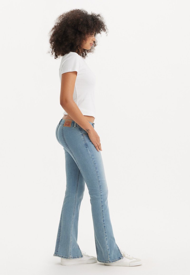 Jean flare bleu clair en denim, avec une taille ajustée et des détails de couture subtils ; associé à un t-shirt blanc à manches courtes.