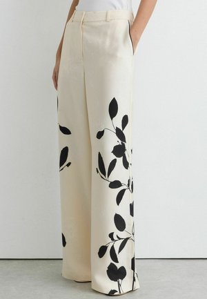 Roomy, crèmekleurige broek met zwarte botanische bladprints, zijzakken en een hoge taille, gecombineerd met een ingestopt wit shirt.