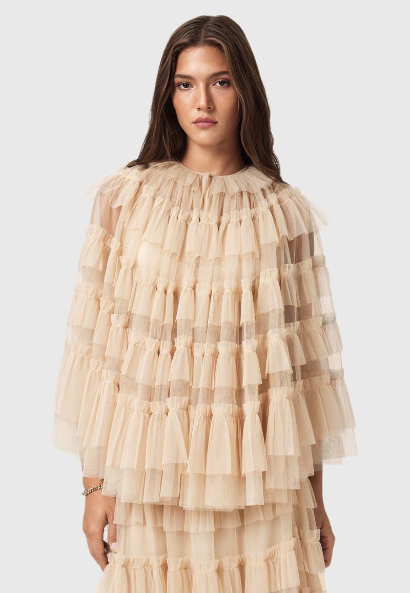 Beige tulle topp med lager av volanger, mjuk textur och hög halsringning. Halvtransparenta ärmar ger en luftig känsla.