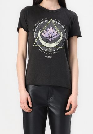 Vrouw draagt een zwarte T-shirt met een centrale afbeelding van een paarse lotus, halve maan, driehoek en tekst over energie en kracht.