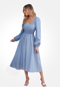 Vestido midi azul con mangas largas tipo globo, escote cuadrado y cuerpo fruncido. Presenta rayas verticales blancas y un dobladillo fluido. Sandalias plateadas.