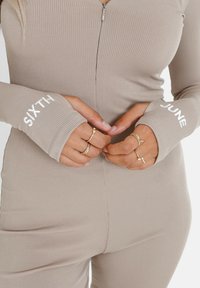 Body de canalé beige con cierre frontal, que presenta bordados en los puños con el texto "SIXTH" y "JUNE", destacando su diseño ajustado.