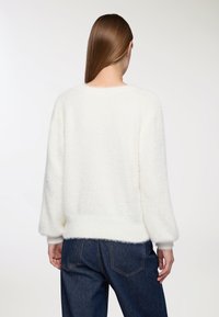 Puszysty biały sweter o luźnym kroju, szerokich rękawach i ściągaczu. W połączeniu z ciemnymi dżinsami, które prezentują miękką teksturę.