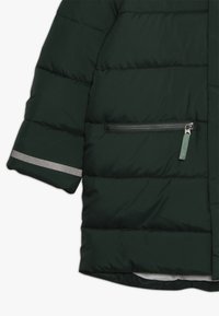 Giacca puffer verde scuro con cuciture orizzontali, tasca con zip e dettaglio riflettente sulla manica. Texture morbida e liscia.