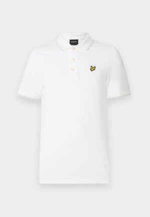Vit polotröja i bomull med texturerad yta. Har en gul broderad logotyp på bröstet, två knappar i placket och kontrasterande krage.