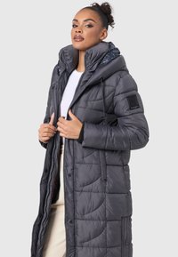 Long, gray puffer coat featuring a quilted design, high collar, and drawstring hood; equipped with a zip closure and side pockets.