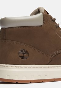 Hnědé semišové vysoké tenisky s krémovým umělým koženým patkem, prošívanými detaily a černým logo stromu na boku. Texturovaná gumová podrážka.