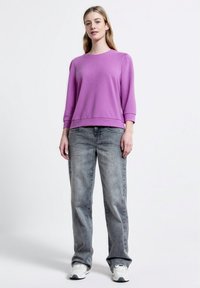 Felpa viola con maniche a tre quarti, vestibilità comoda e colletto a costine, abbinata a jeans dritti grigi chiari e sneaker bianche.