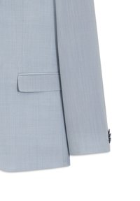 Μανίκι σακακιού σε ανοιχτό μπλε με λεπτομέρεια σε τσέπη με καπάκι και διακριτή υφή, με ορατά κουμπιά στη μανσέτα, σε λευκό φόντο.