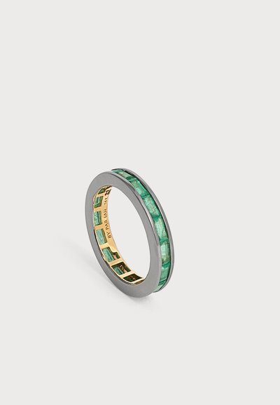 Bague en argent et or avec des pierres précieuses rectangulaires vertes incrustées autour du tour, présentée sur un fond clair uni.