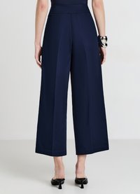 Pantalon large marine avec un tissu lisse, deux plis verticaux à l'avant et une taille haute. Associé à des sandales noires à talons.