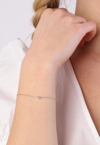 Zilveren schakelarmband met een klein rond accent, gedragen om een pols, met een delicaat ontwerp en een gladde oppervlaktestructuur.