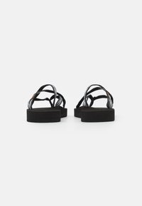 Black platform sandals with crisscross straps. The material is textured, featuring a smooth base and a subtle sheen on the straps.