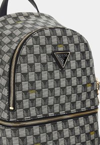 Zaino in bianco e nero con stampa geometrica e hardware dorato, caratterizzato da una finitura testurizzata, una parte superiore arrotondata e un accento logo triangolare.