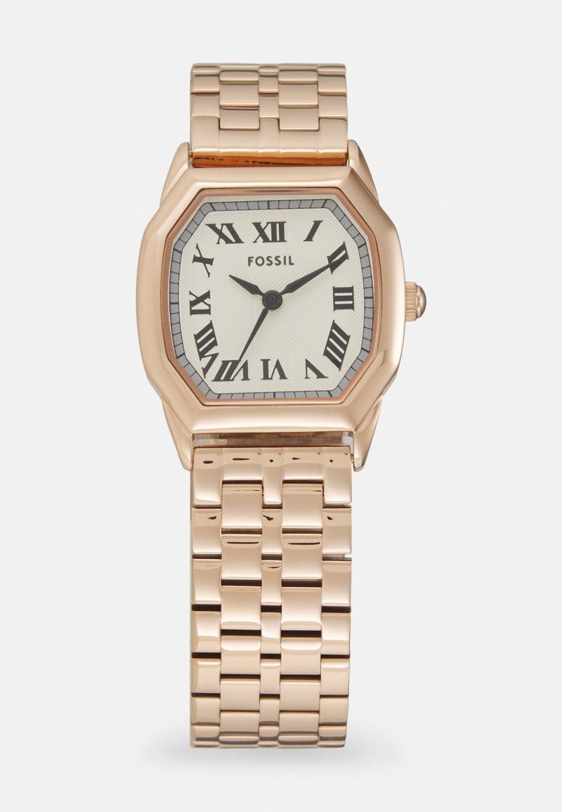 Montre octogonale en or rose Fossil avec un cadran blanc texturé, des chiffres romains noirs et un bracelet en maillons métalliques. Elle présente un fermoir simple.