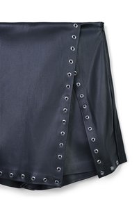 Schwarzer Kunstleder-Minirock mit silbernen Metallösen entlang der gewickelten vorderen Kanten und dem unteren Saum, vor einem weißen Hintergrund.