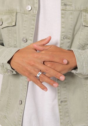 Silver metal ring with a black accent, worn on a hand. Hands are relaxed, with a light-colored denim jacket over a white shirt.