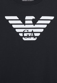 Zwart katoenen t-shirt met een wit adelaarslogo met horizontale strepen en de letters "GA" gecentreerd eronder.