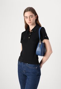 Svart polo skjorte med gullknapper, korte ermer og rett skjæring, kombinert med blå denimjeans og en blå håndveske.