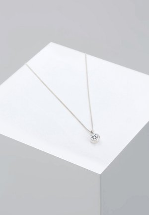 Silberne Kette mit einem runden Anhänger, der einen klaren Edelstein zeigt, auf einer weißen Präsentationsfläche liegend. Einfaches Kettendesign, polierte Oberfläche.