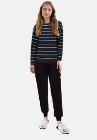 Schwarz-gestreifter Sweatshirt mit grauen Streifen und gerippten Bündchen, kombiniert mit schwarzen, strukturierten Jogginghosen und flauschigen weißen Hausschuhen. Lässiges Loungewear-Outfit.