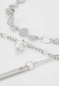 Sidabrinė grandinėlė su apvaliais ir ovaliais diskai; įtrauktas perlas ir elegantiškas stačiakampis žavesys. Lygūs, atspindintys paviršiai.