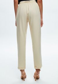 Pantalon beige clair à taille élastique, doté d'une coupe décontractée et de jambes droites, avec des revers aux chevilles. Texture lisse.