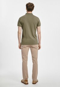 Oliwkowa koszulka polo z krótkim rękawem, z prążkowanym kołnierzykiem i beżowymi wykończeniami, w połączeniu z jasnobeżowymi spodniami oraz brązowymi butami wsuwanymi.
