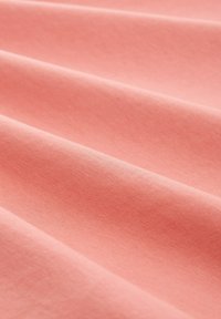 Světle růžová látka s jemnou, hladkou texturou a záhyby, která ukazuje její lehký a elastický materiál. Žádné vzory ani kovové prvky nejsou vidět.