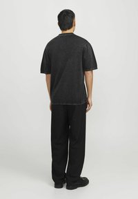 Chemise en denim noir à manches courtes, coupe décontractée, coutures visibles, associée à un pantalon noir ample et des chaussures noires.