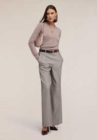 Maglione di lana rosa chiaro, pantaloni larghi grigi a righe sottili, cintura bordeaux con fibbia circolare, décolleté bordeaux e una borsa beige strutturata.