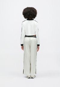 Λευκό cropped σακάκι με μαύρες λεπτομέρειες, συνδυασμένο με ανοιχτόχρωμο κάτω μέρος με πλαϊνές σχισμές. Ομαλή υφή, αθλητικός σχεδιασμός και λεπτομέρειες με λογότυπο.