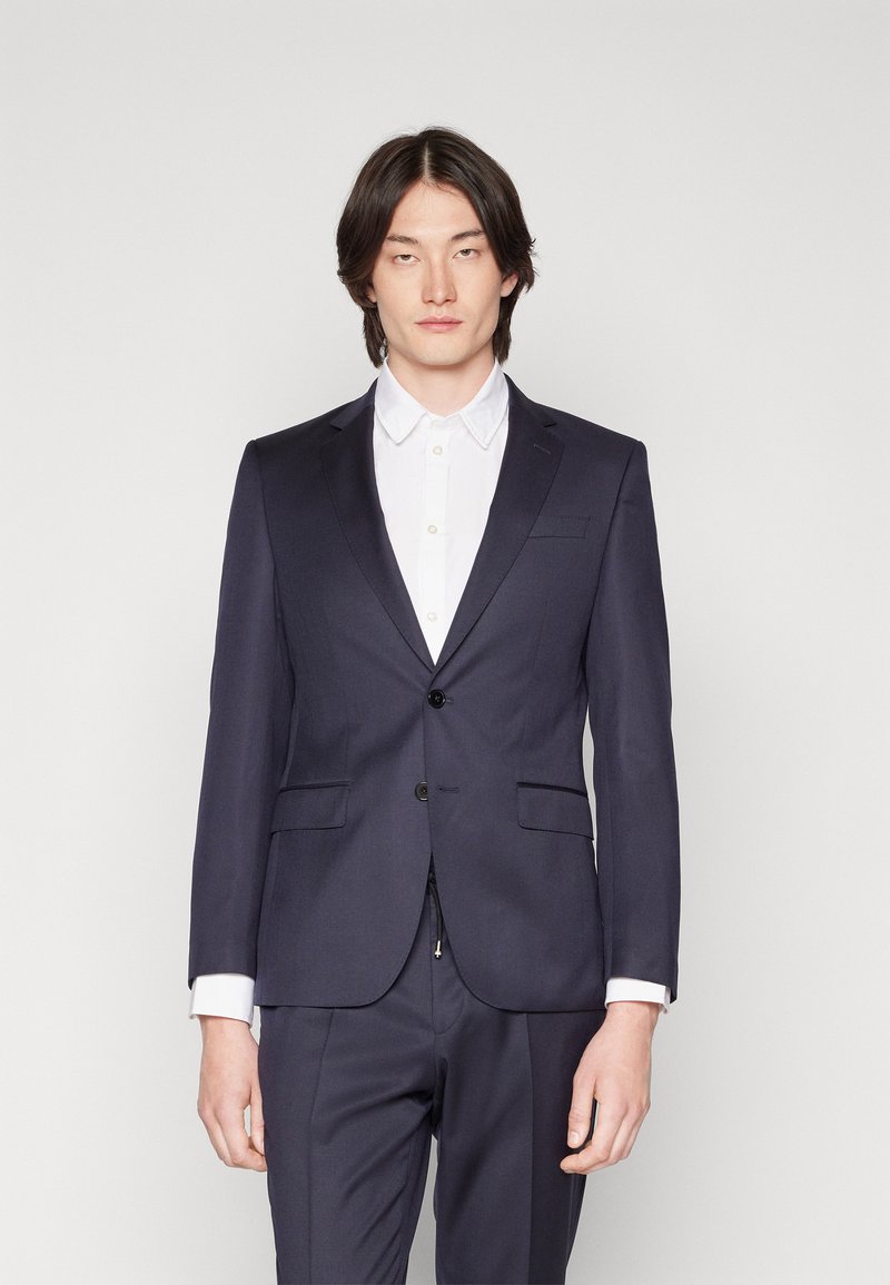 Marineblauwe blazer met een notched lapel en enkele knoopsluiting, gecombineerd met een witte overhemd met kraag. Smooth stof, minimalistisch ontwerp.