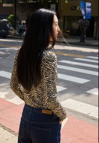 Maglietta a maniche lunghe con stampa zebrina bianca e nera, abbinata a jeans in denim a vita alta con un'etichetta in pelle che reca la scritta "ICHI".