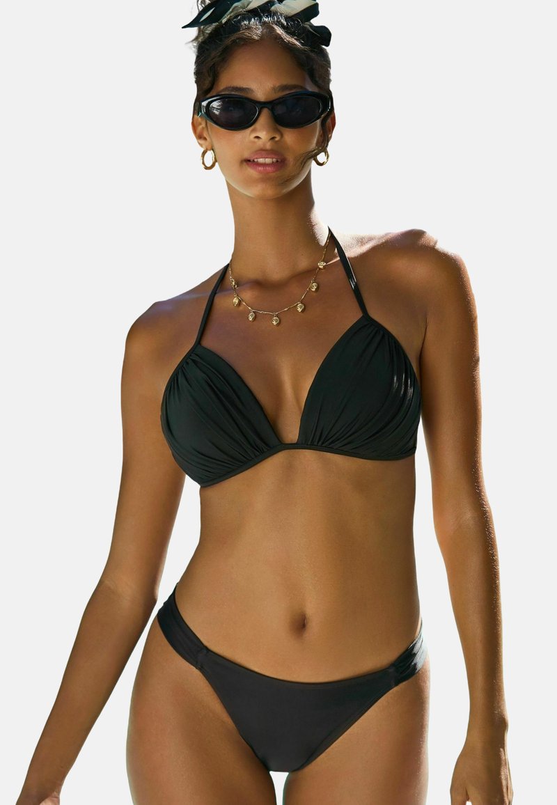 Juodas bikinis, kuris turi trikampio formos viršutinę dalį su suplėšyta medžiaga ir plonomis dirželių, derinamas su žemais bikini apatiniais. Papuoštas auksiniais papuošalais.
