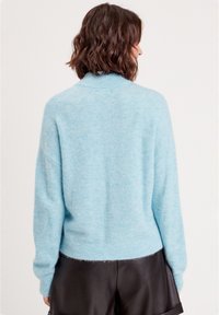 Pull en flanelle bleu clair avec un col montant et un ourlet côtelé ; il possède des épaules tombantes et des manches longues, associé avec un short noir.