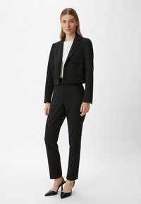 Zwarte cropped blazer met notch-lapels over een witte top, gecombineerd met op maat gemaakte zwarte broek en puntige zwarte hakken; gladde stof, minimalistisch ontwerp.