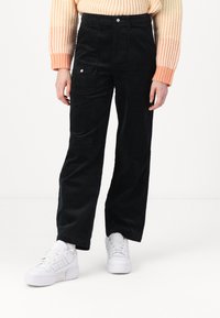 Mustad corduroy püksid sirge säärega, suurte esipocketitega ja peene tekstuuriga. Kombineeritud valgete tossudega.