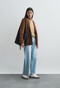 Brun kordfløyelsblazer, beige genser med høy hals, lyseblå vid bukse, hvite sneakers med brune detaljer, og en svart skulderveske.