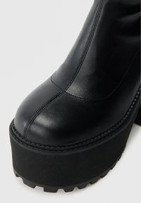 Čierna kožená členková čižma s okrúhlym špičkou, rebrovanou textúrou a robustnou platformovou podrážkou. Má viditeľné švy a matný povrch.