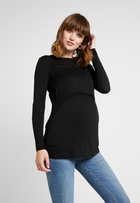 Top de maternidade preto de mangas longas com um design curvado na cintura, feito de um tecido suave; combinado com jeans azuis. Textura suave, estilo ajustado.