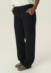 Black tailored pants with a straight leg design, featuring two side pockets and a smooth fabric texture. Worn with brown loafers.