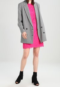 Overdimensionerad kavaj i houndstooth-mönster, rosa spetsklänning med scallopad nederkant och svarta öppna ankelstövlar med blockklackar.