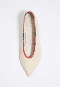 Zapato plano de cuero beige con punta afilada, adornado con un ribete de patrón rojo y negro alrededor de la abertura y una plantilla texturizada.