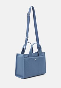 Sac à main rectangulaire en tissu bleu avec deux petites poignées, une longue bandoulière réglable et une poche extérieure avec bouton pression.