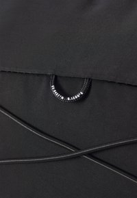 Black fabric with a smooth texture features a drawstring loop and contrasting curved stitching lines. The design is streamlined and minimalistic.