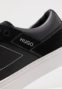 Sneaker nera realizzata in suede e materiale sintetico, con cuciture bianche e un logo. Design a profilo basso con suola in gomma bianca.