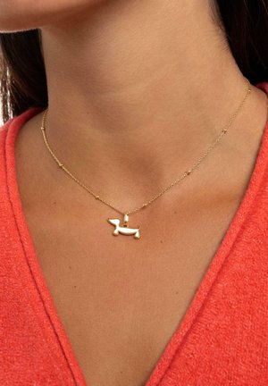 Collana in oro con un pendente a forma di bassotto, dalla finitura lucida, indossata su una maglietta color corallo.