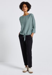 Top azzurro chiaro con scollo ampio, maniche a tre quarti e orlo regolabile con coulisse, abbinato a pantaloni neri tapered e sneakers bianche.