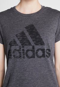 Mørkegrå kortærmet t-shirt lavet af blødt stof, med et stort sort Adidas-logo på forsiden. Tekstureret, afslappet design.
